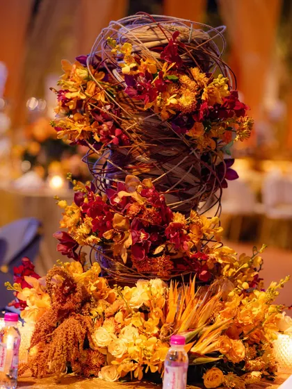 A detailed close-up of the woven midollino structure, revealing the intricate craftsmanship involved. The warm-toned flowers are artfully placed to create a sense of movement and energy.