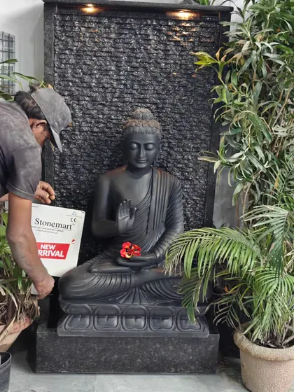An artisan makes a final touch, adding a flower to the 3-foot black marble Buddha statue. This piece is set against a 5-foot ribbed granite waterfall, combining spiritual art with modern design.