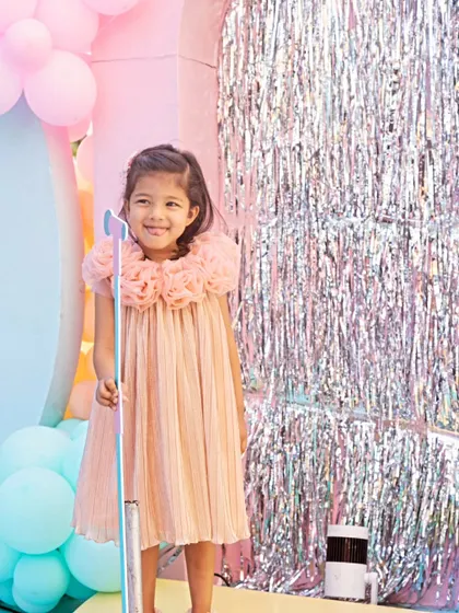 The birthday girl smiles brightly in front of a shimmering silver tinsel backdrop, holding a prop microphone. This photo booth moment perfectly captures the fun and playful spirit of her party.