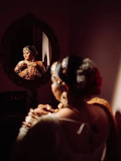 A moody and artistic bridal portrait using a mirror. The play of light and shadow, with the bride's reflection in sharp focus, creates a sense of introspection and beauty.