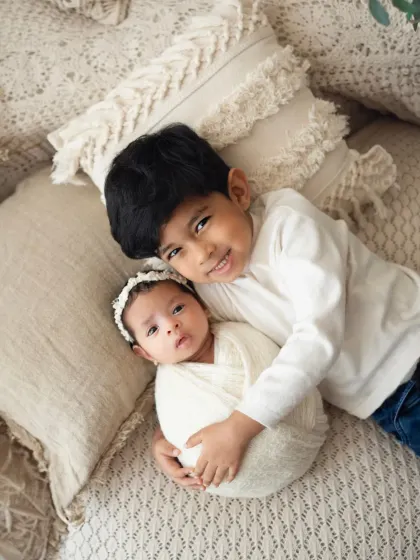 An adorable overhead shot of a big brother cuddling his newborn sister. She looks right at the camera, making for a precious and engaging portrait.