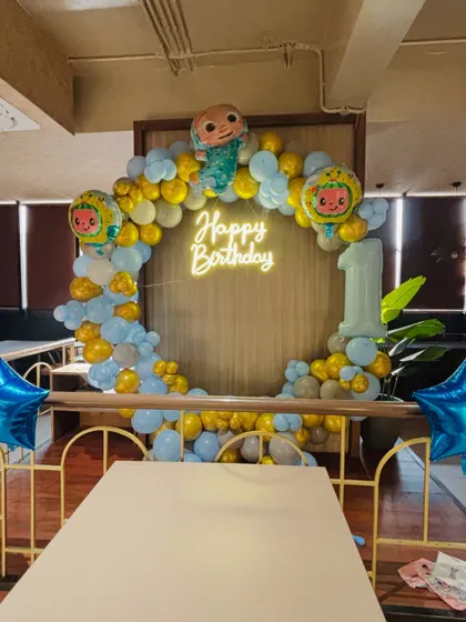A Cocomelon-themed first birthday party. This popular theme includes a circular balloon arch, a 'Happy Birthday' neon sign, and Cocomelon character foil balloons.