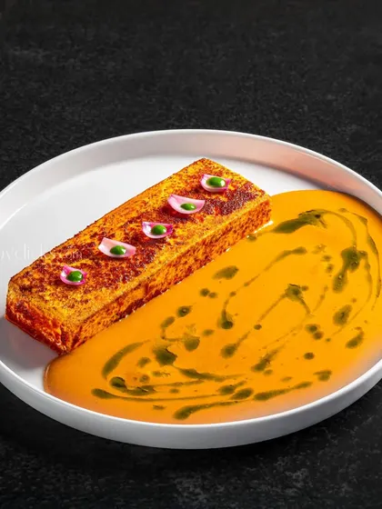 A modern vegetarian dish with a savory cake in a creamy yellow sauce, demonstrating artistic plating.
