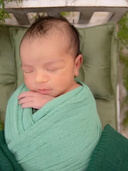 A close-up of a newborn wrapped in a beautiful shade of green. The focus is on the baby's serene expression and the texture of the swaddle.
