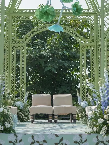 The couple's seating inside the mandap, surrounded by lush arrangements of blue and white flowers, creating an intimate and beautiful ceremony space.
