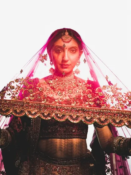 A powerful portrait of the bride, Khushi, holding her veil, with dramatic lighting creating a striking image.
