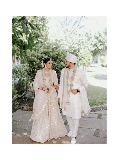 A happy, walking portrait of Jui and Vi in their elegant white wedding attire. Their smiles and the natural green background create a fresh and joyful image.