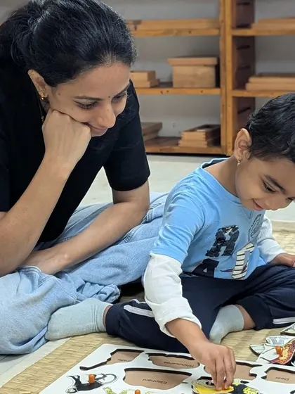 A mother observes with a smile as her son works on a puzzle. This quiet connection gives the child the confidence to explore while knowing support is close by.