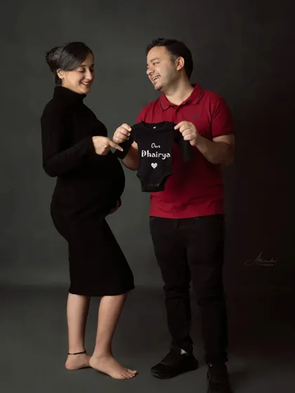A fun and creative announcement. The dad-to-be holds up a personalized baby onesie, a sweet and unique way to share the baby's name.