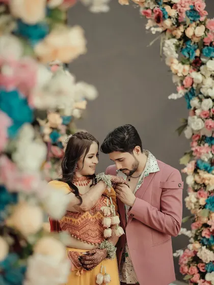 A sweet moment where the groom kisses the bride's hand. This gesture of affection is beautifully framed by the soft, colorful flowers of the decorative arch.