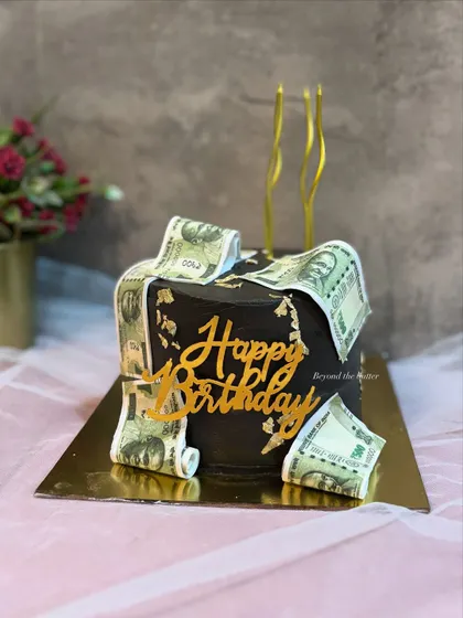 A fun money themed cake for a birthday celebration. This black cake is decorated with edible currency notes and a gold "Happy Birthday" topper.