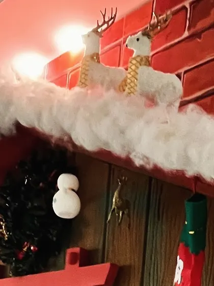A close-up of a Christmas fireplace mantel, decorated with faux snow and white reindeer.