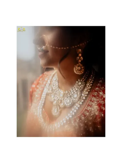 A detail shot of the bride's necklace and the intricate embroidery of her lehenga. The soft, glowing light adds a magical quality to the image.