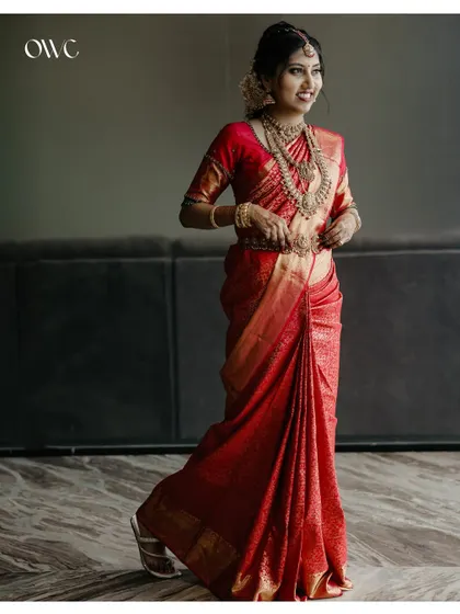 An elegant full-length portrait of the bride, her red saree flowing beautifully.