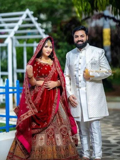 A classic combination featuring a bride in a grand red velvet lehenga and the groom in a sophisticated white sherwani. This pairing is timeless and ensures both partners look equally stunning in traditional pre-wedding photos.