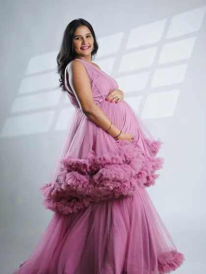 This side profile shot in the pink gown beautifully highlights the curve of the baby bump. The soft window light effect adds a dreamy and gentle quality to the portrait.