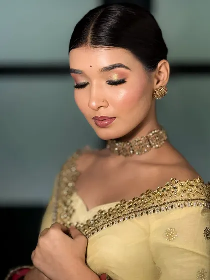 A close-up of the soft glam makeup on the bride in the yellow saree. Her eyes are closed, showcasing the beautiful blend of peachy and gold eyeshadow.