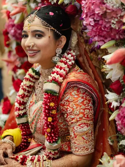 This bride looks radiant and happy on her big day. Her red and gold saree with a custom embroidered blouse is a classic and stunning choice.