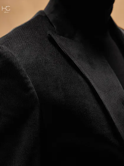 This detail shot of a black corduroy suit jacket highlights the fine texture of the fabric and the sharp peak lapel. It’s a look that speaks of depth and substance.