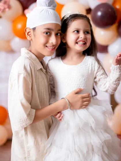 A bright, happy photo of a brother and sister sharing a hug. Their joyful expressions and the festive balloon background make this a perfect celebration shot.