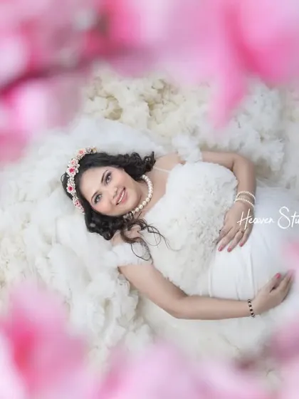 Dreaming of the little one. This creative shot, framed by soft pink flowers, captures the mother-to-be in a moment of serene contemplation, looking absolutely angelic in a white ruffled dress.