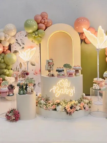 A custom "Oh Baby" party with a butterfly theme in soft, earthy tones. The glowing butterfly lamps and floral arrangements around the cake table create a stunning focal point.