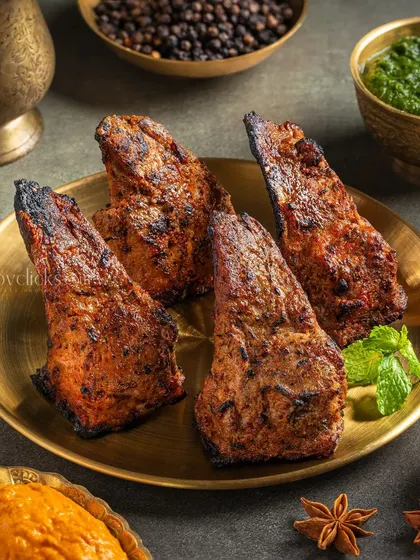 Charred and flavorful mutton chaap (ribs), presented on a brass plate with whole spices.