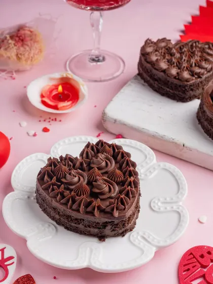 A heart-shaped chocolate mini cake for Valentine's Day, with intricate piping, styled on a flower-shaped plate.