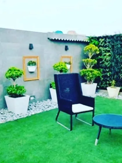 A stylish rooftop lounge area. It features an artificial grass floor, a vertical garden wall, and decorative touches like framed wall planters and topiary trees.