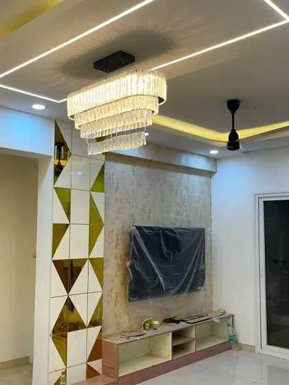 A living room under construction, showing the installation of a grand crystal chandelier and a geometric mirrored partition wall, hinting at the luxurious final design.