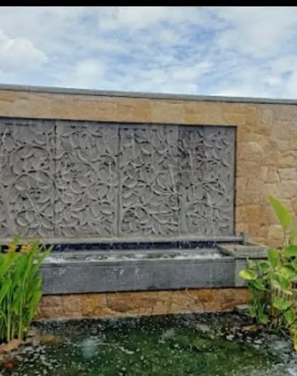 A daytime view of a custom stone waterfall feature with a carved panel, set within a stone-clad wall. This type of water feature becomes a natural and calming focal point in any garden.