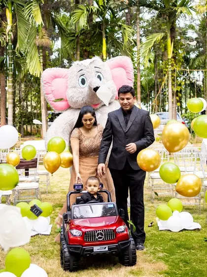 The birthday boy, Shourya, making a grand entrance in a toy car, accompanied by his parents and a large elephant mascot.