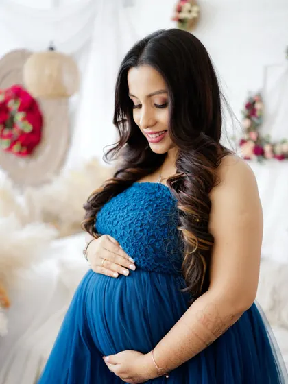 A close-up portrait capturing the pregnancy glow. The mom-to-be looks down at her bump with a gentle smile, dressed in a beautiful blue gown.