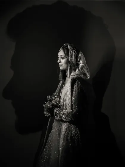 A powerful and artistic silhouette portrait. The bride stands in the foreground, her form illuminated, while the groom's profile is cast as a strong shadow behind her, symbolizing their deep connection.
