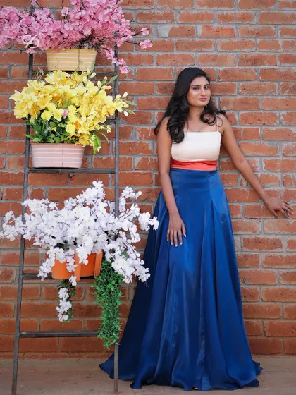 My client poses gracefully in her custom pre-wedding shoot dress, featuring a color-blocked design with a white tube top, orange belt, and a royal blue satin skirt.