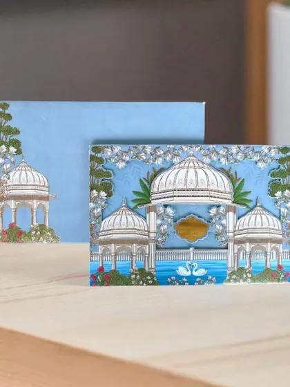 This Pichwai-themed invitation showcases the serene beauty of traditional Rajasthani art. The design features elegant pavilions and swans, set against a calm blue, perfect for a classic and artistic wedding.