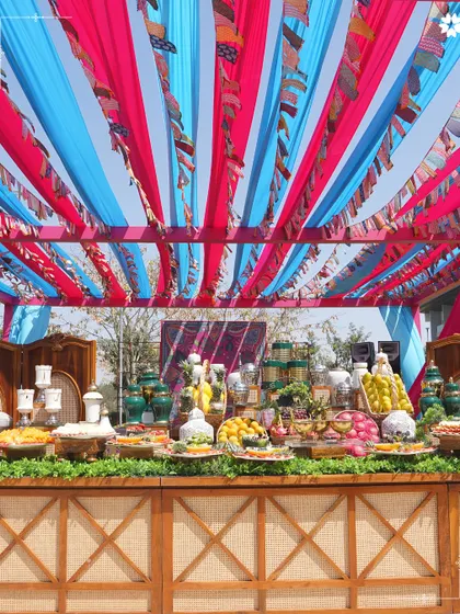A vibrant fruit and cheese bar at a destination wedding in Bengaluru. The colorful canopy and rustic wooden counter create a festive, market-like feel, offering guests a fresh and interactive culinary experience.