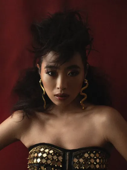 A dramatic hair and beauty shot against a rich red background. The focus is on the sculptural hairstyle and the model's intense expression.