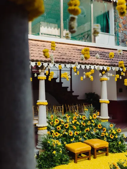 A view of the Haldi setup from the side, showing the traditional architecture of the venue decorated with hanging marigold strings and a sunflower-filled stage.