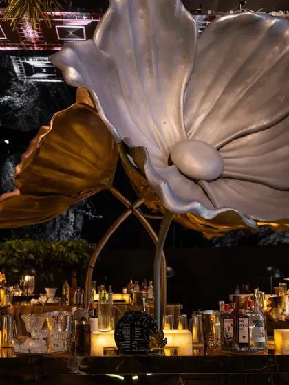 A massive, sculptural lotus flower in silver and gold, positioned over the bar. This statement piece is both a light fixture and a work of art, defining the event's aesthetic.