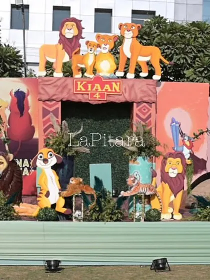 The main stage for a 'Lion King' themed birthday party, featuring a massive backdrop with all the beloved characters from the Pride Lands. The setup includes animal props and balloon garlands in earthy tones.