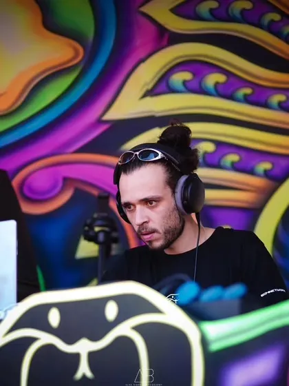 A DJ focused on his mix, framed by the colorful, psychedelic art of the stage. This is a great example of capturing performers in their creative zone.
