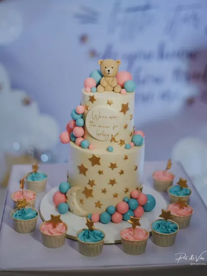 A full view of the adorable baby shower cake and matching cupcakes we created for Drashti Dhami. The design features a soft color palette, stars, a crescent moon, and a cute teddy bear.