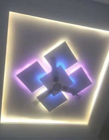 A central fan fixture is surrounded by floating squares with dual-color backlighting. The outer cove light provides a warm, uniform glow.