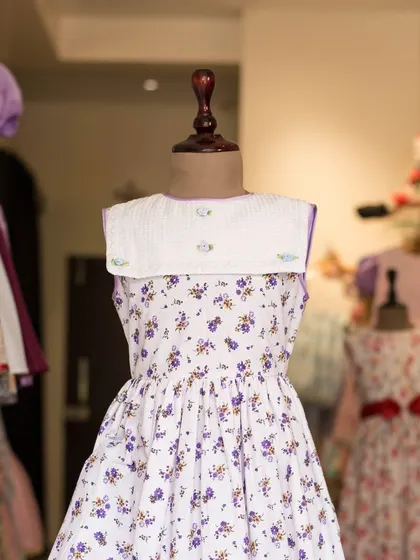 A lovely white dress with a delicate purple floral print. The sailor-style collar in a textured white fabric adds a touch of vintage charm.