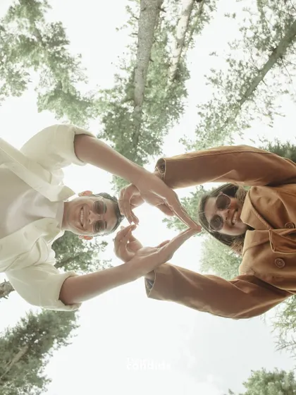 A creative, low-angle shot of the couple making a heart shape with their hands against the sky and trees. It’s playful, joyful, and unique.