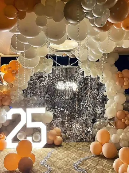 A glamorous 25th birthday celebration. This stunning setup features a ceiling full of balloons, a silver shimmer wall, and a large light-up number '25'.