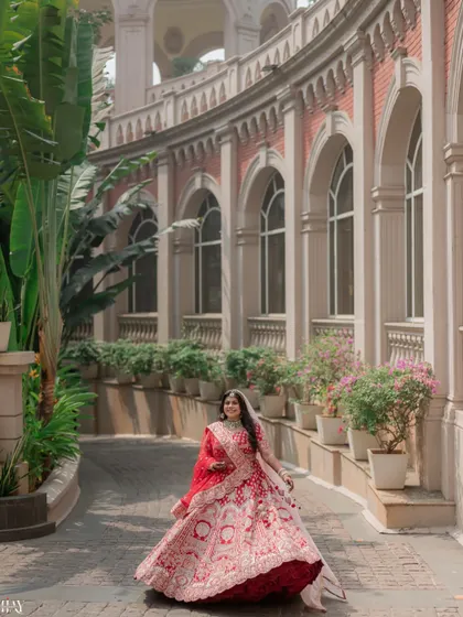 The bride walks through a beautiful arched corridor, her red lehenga creating a stunning visual.