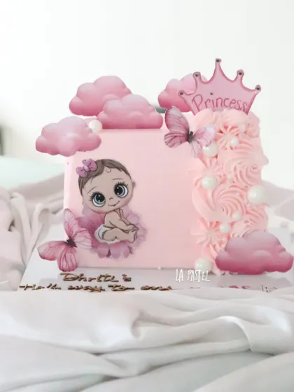 A pretty pink half-birthday cake for a little princess. This square cake features a cute baby illustration, fluffy pink clouds, butterflies, and a princess crown topper.
