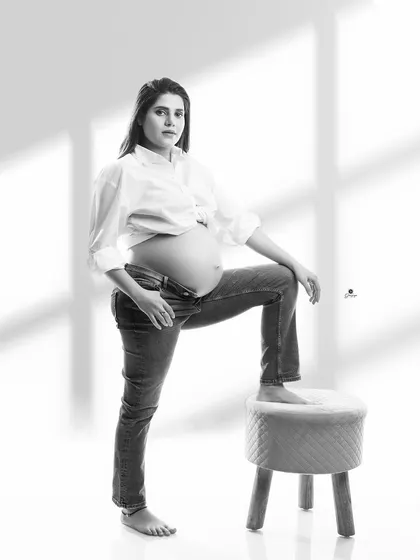 A confident and modern black and white portrait. The client's pose, with an open shirt and jeans, creates a stylish and bold image that celebrates the pregnant form.